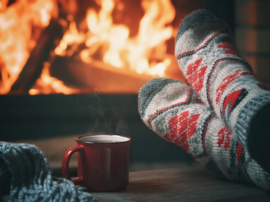 A person's feet in cozy socks and a coffee mug in front of a fire